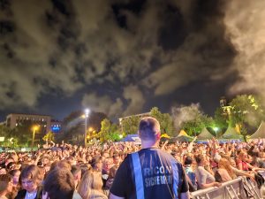 Sicherheitsmitarbeiter der Firma RICON überwacht von einem erhöhten Punkt die Zuschauermenge beim Stadtfest Mannheim 2024. Es ist dunkel und die Zuschauer feiern. Veranstaltungsschutz. Eventschutz. Bühnenbewachung.